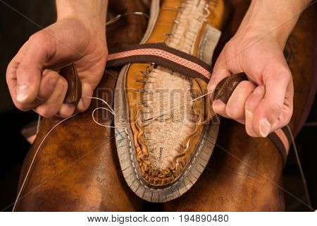 Cropped image of bootmaker sitting in workshop making shoes