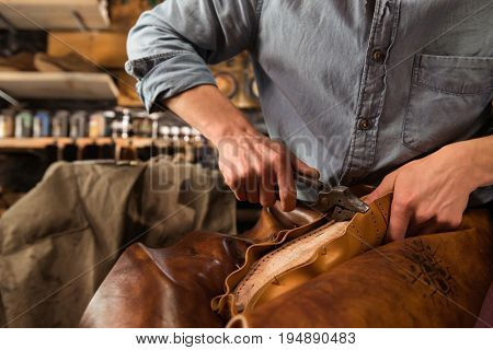 Cropped image of bootmaker sitting in workshop making shoes