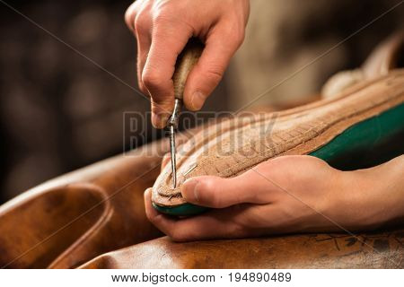 Cropped image of bootmaker sitting in workshop making shoes