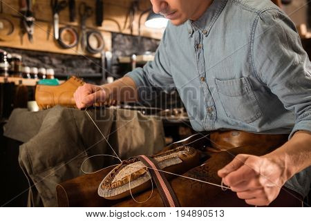 Cropped image of bootmaker sitting in workshop making shoes