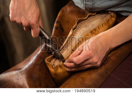 Cropped photo of bootmaker sitting in workshop making shoes