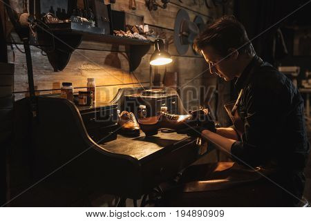 Picture of young concentrated man shoemaker at footwear workshop.