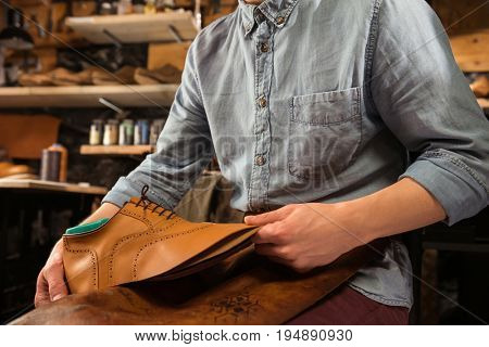 Cropped image of bootmaker sitting in workshop making shoes
