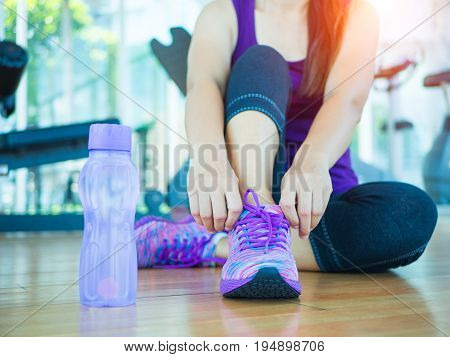 Running shoes - closeup of woman tying shoe laces. Female sport fitness runner getting ready for jogging in gym room with fitness equipments in backgroound