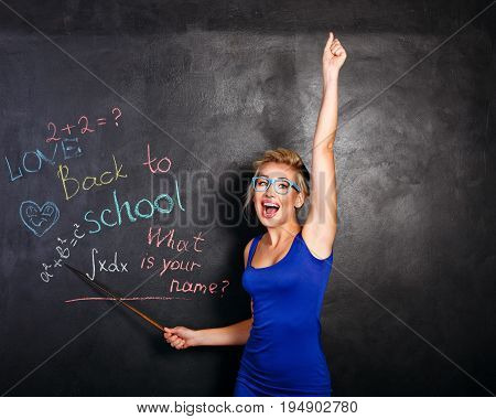 Young attractive student at the school board. She rejoices at the beginning of the school year and holds a pointer in her hands. Back to school. She welcomes new students.