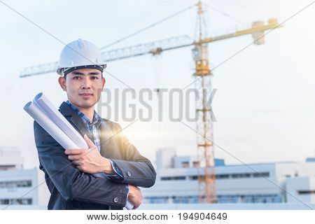 The architect wear white safety helmet and hold the blueprint with commitment on construction site with crane background