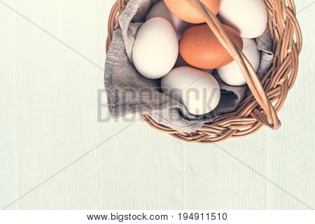 Basket with white and brown natural eggs on white wooden background