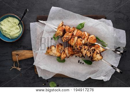 Barbecued chicken breast skewers with avocado sauce on dark background top view