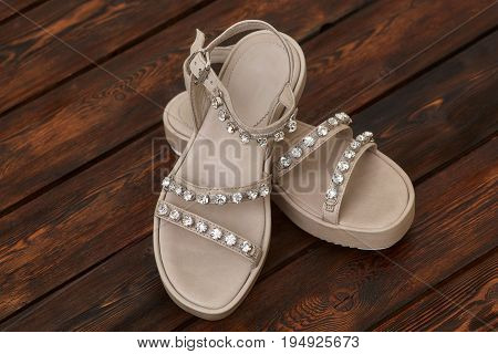 Pair of beige leather female sandals with rhinestones on wooden background