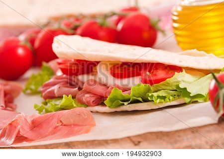 Piadina with ham and lettuce on wooden table.