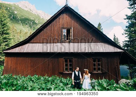 the bride and groom standing near the wooden house in the mountains