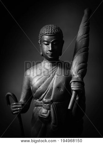 Black and white photo of Buddha statue hold umbrella and stave.