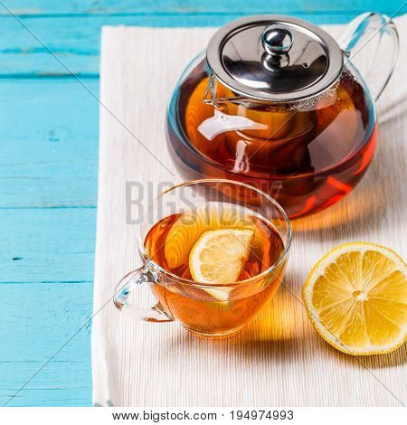 Glass cup of tea with lemon and glass teapot on blue wooden table.