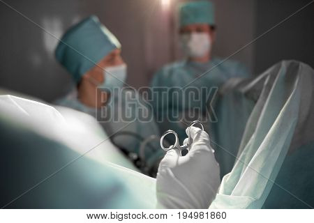 Selective focus on surgical instrument in the hands of a professional surgeon during surgery in operating theatre of the hospital medical team performing operation on the background.