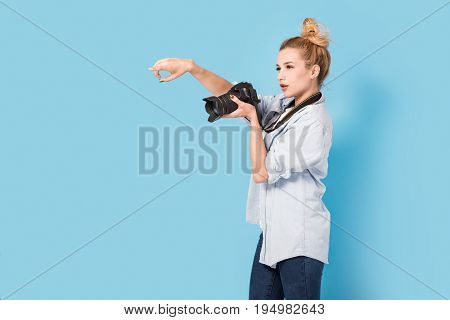 Woman Blonde Photographer Shows How To Pose To Somebody. Model Isolated On A Blue Background With Co