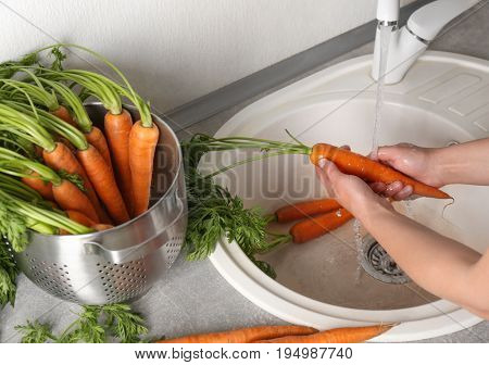 Woman washing fresh carrots in kitchen sink