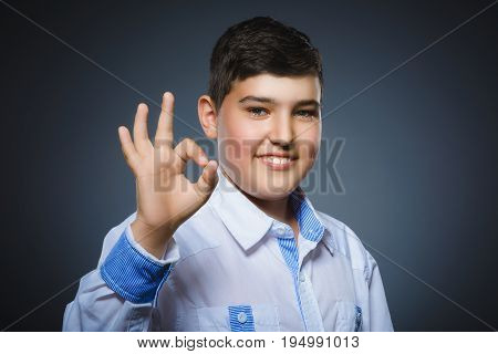 Happy boy. Closeup Portrait of handsome teenager smiling and show Ok over grey background.