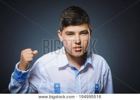 Portrait of angry boy isolated on gray background. He raised his fist to strike.