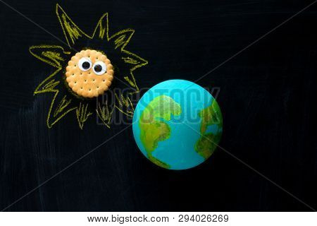 Top View  Handmade Model  Of Earth Planet  And Cookie Sunwith Funny Googly Eyes  On The Chalkboard ,