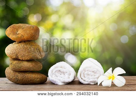 Stack Of Stone And White Towel With Flower On Wooden Floor On Green Bokeh Background, Spa Concept