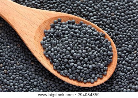 Black Beluga Lentils In A Wooden Spoon On Black Beluga Lentils Background. Close-up.