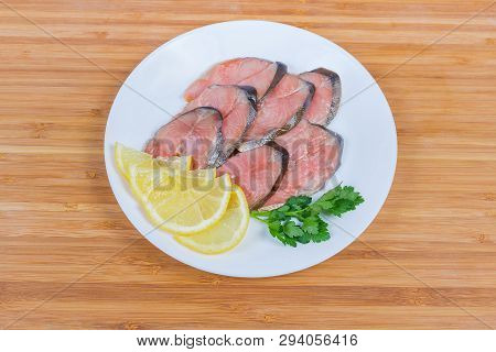 Slices Of Smoked Pink Salmon, Lemon Slices And Parsley Twig On White Dish On The Wooden Bamboo Surfa
