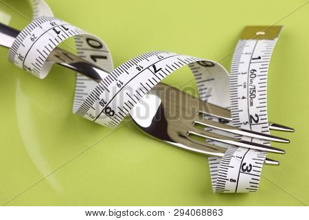Diet Concept. Tape Measure Wrapped Around The Fork On A Green Plate. Close-up.