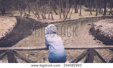 Young Boy Standing On The Wooden Bridge And Enjoying The Picturesque View Of The River.