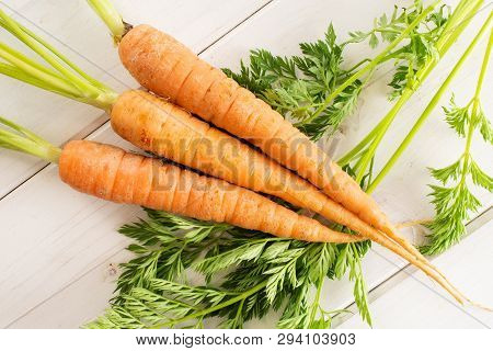 Group Of Three Whole Fresh Orange Carrot With Greens Flatlay On White Wood