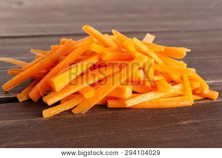 Lot Of Pieces Of Fresh Orange Carrot Cut Into Thin Noodles On Brown Wood