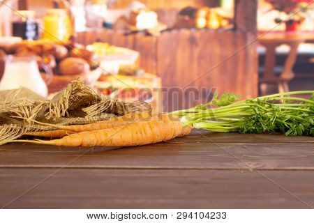 Group Of Three Whole Fresh Orange Carrot With Greens And A Jute Bag In A Rustic Kitchen