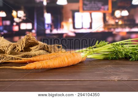 Group Of Three Whole Fresh Orange Carrot With Greens And A Jute Bag In A Restaurant