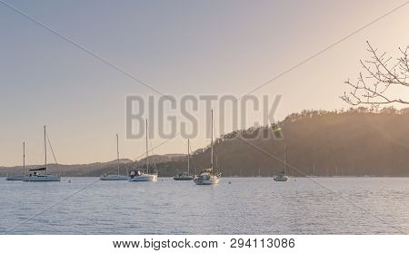 Sailing Boats Sit Stationary On Lake Windermere - Lake District, Cumbria - During An Early Spring Su