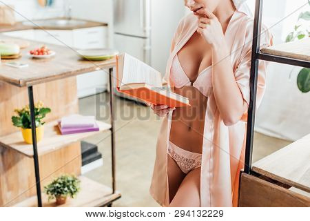 Cropped View Of Sexy Girl In White Lingerie And Housecoat Reading Book In Kitchen