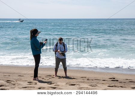 Malibu, California - March 26, 2019: Adult Tourists Fuss And Play With Their Phones While Enjoying T
