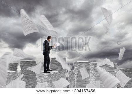 Businessman At Work Over A Pile Of Paper Towers Of Worksheets