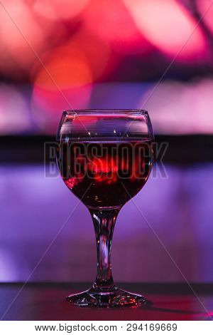 A Glass Goblet With A Red Drink Stands On The Table On A Blurred Background