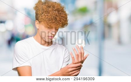 Young handsome man with afro hair wearing casual white t-shirt Suffering pain on hands and fingers, arthritis inflammation