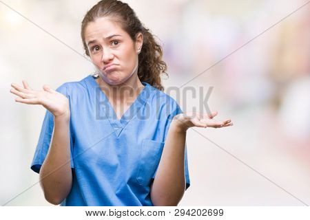 Young brunette doctor girl wearing nurse or surgeon uniform over isolated background clueless and confused expression with arms and hands raised. Doubt concept.