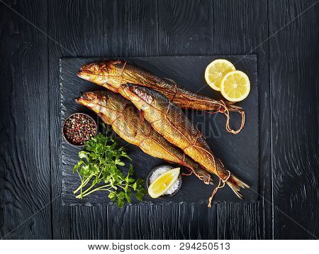 Three Hot Smoked Herrings On A Black Slate Tray With Lemon Slices, Parsley And Peppercorns, View Fro