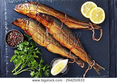 Three Hot Smoked Herrings On A Black Slate Tray With Lemon Slices, Parsley And Peppercorns, View Fro