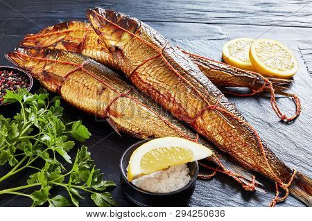 Freshly Smoked Whole Herrings With Lemon Slices, Parsley And Peppercorns On A Black Slate Tray  On A