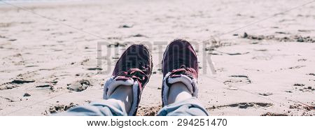 Feet Of Young Woman In Sport Footwear And Jeans Relaxing After Hiking On Sand Beach. Pov. Adventure 