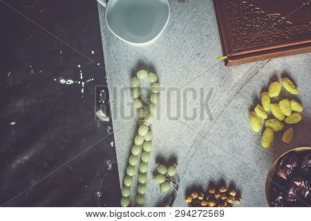 Holy Quran, Rosary, Iftar Sweets And Dried Fruits With A Cup Of Water. View From Above. Flat Lay Pho