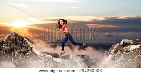 Redhead Woman Jumps Through The Gap Between Hills Over Cliff On Blue Sky Background.