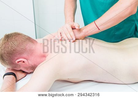 Patient Receiving Massage From Therapist. A Chiropractor Does Deep Tissue Massage On Man's Shoulder 