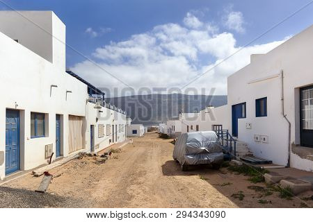 Empty Street With Sand And White Houses And A Car Covered With Plastic In Caleta De Sebo On The Isla