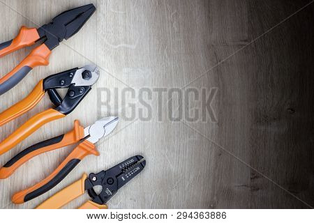 Set Of An Orange And Black Pliers, Stripper And Edge Cutter Isolated On A Wooden Background.