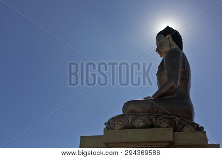 Buddha Dordenma statue silhouette on blue sky background with sun halo around its head in Thimphu, Bhutan
