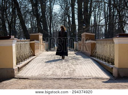 Girl In A Leather Jacket And Black Skirt Goes Over An Old Bridge.